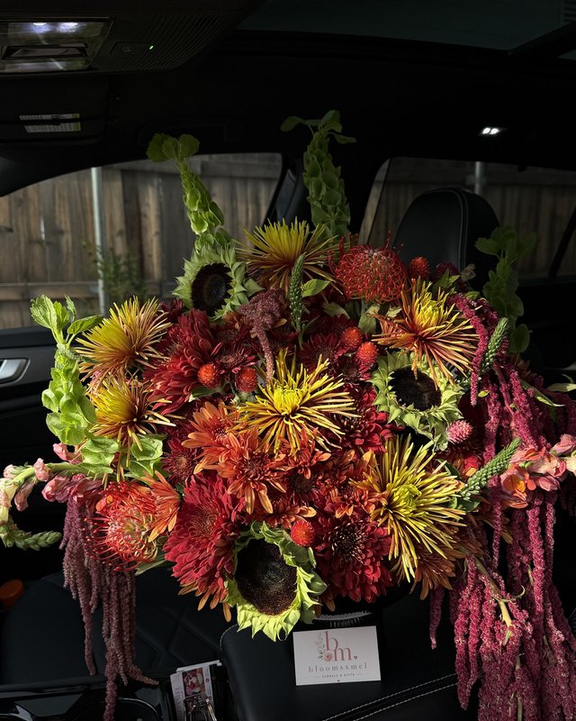 Cosecha by Blooms x Mel — Spider mums, dark-center sunflowers, pincushion protea, and hanging amaranthus in a footed vase