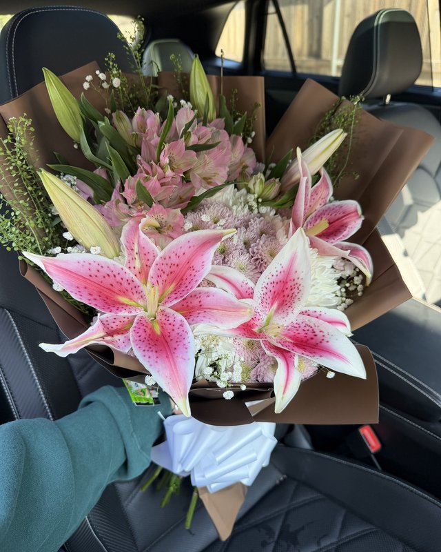 Estrella Rosa by Blooms x Mel — Stargazer lilies rising over a soft bed of mums, alstroemeria, and baby's breath in a warm brown wrap