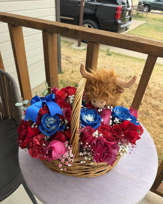 La Vaquita by Blooms x Mel — Red and blue roses with baby's breath in a wicker basket, topped with a plush highland cow